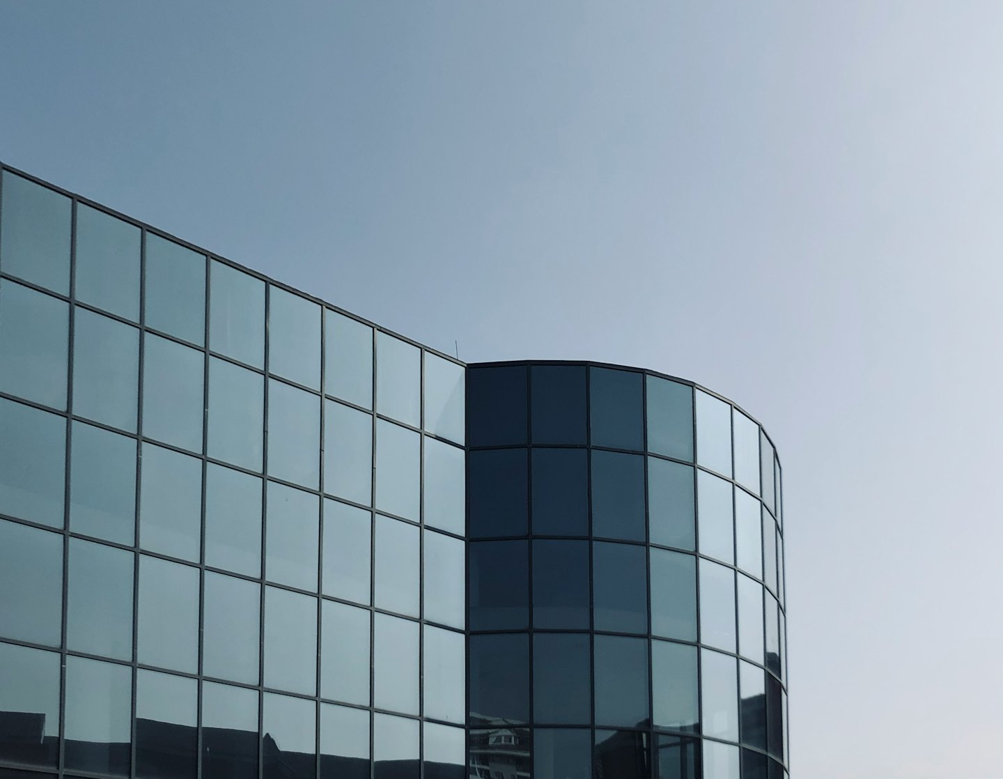 Modern glass office building with curved corners against a clear sky.